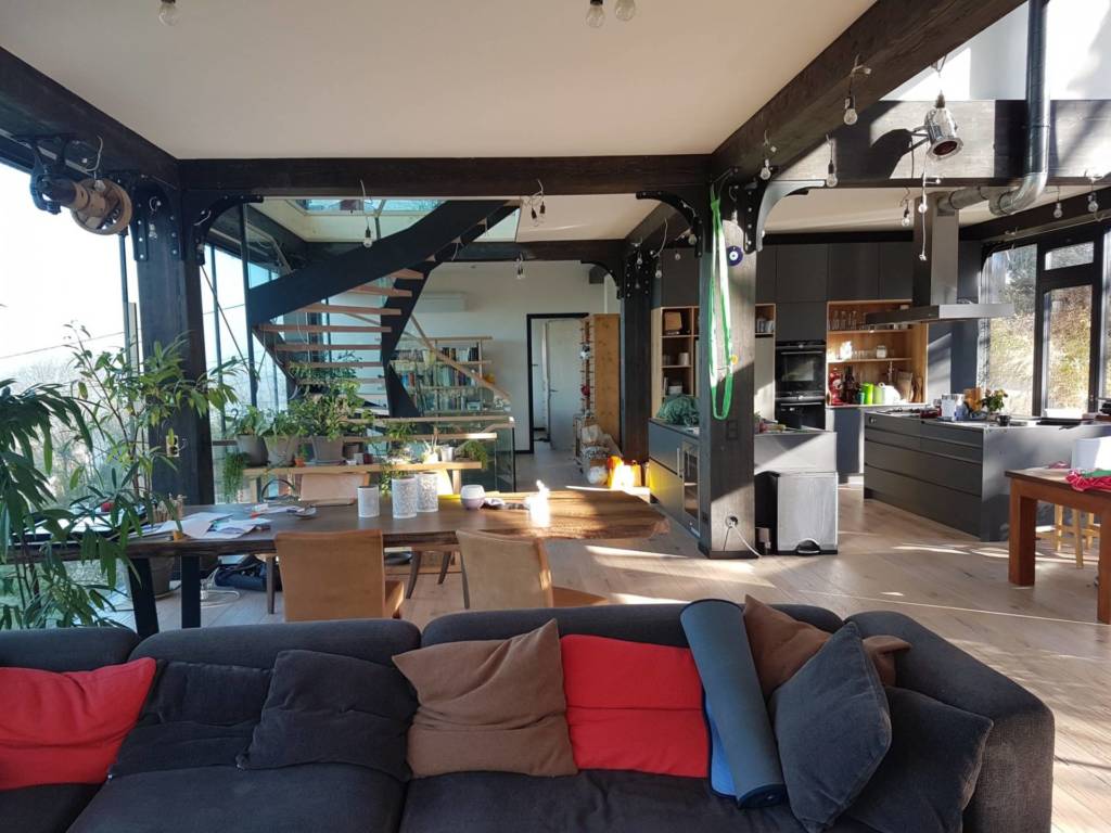 helles Wohnzimmer mit offener Küche und vielen Fenstern.