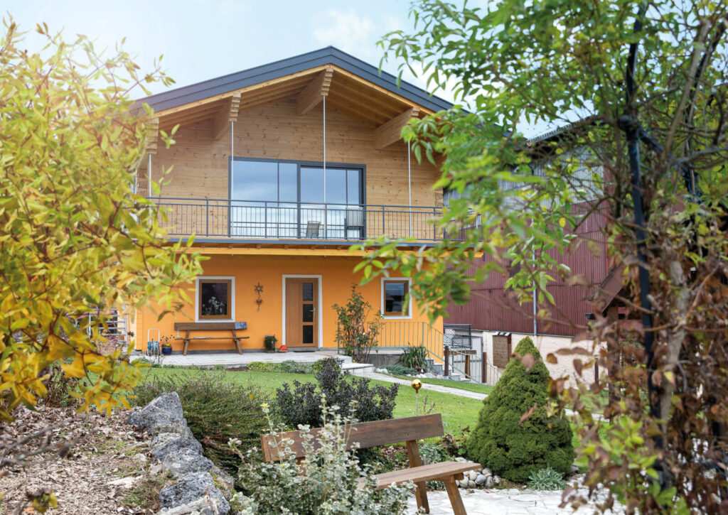 klassisches Haus mit Holzverblendung der oberen Etage und auffälligem orangen Anstrich der Fassade und Garten.